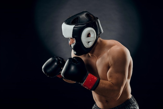 Portrait of a young man with a Boxing helmet and gloves on a dark background