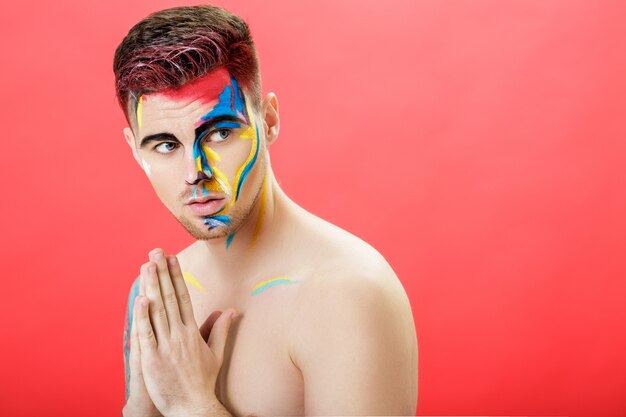 Portrait of a young man with colored face paint on a red background