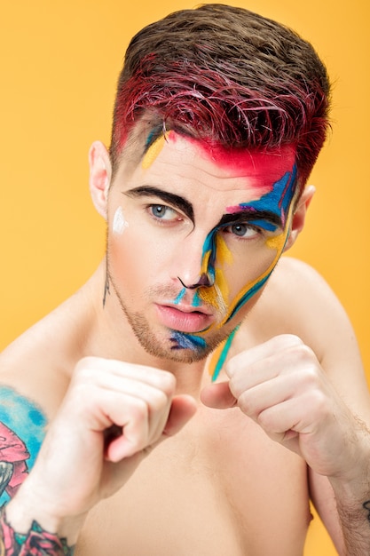 Portrait of a young man with colored face paint on a yellow background