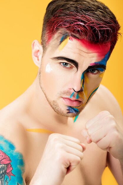 Portrait of a young man with colored face paint on a yellow background