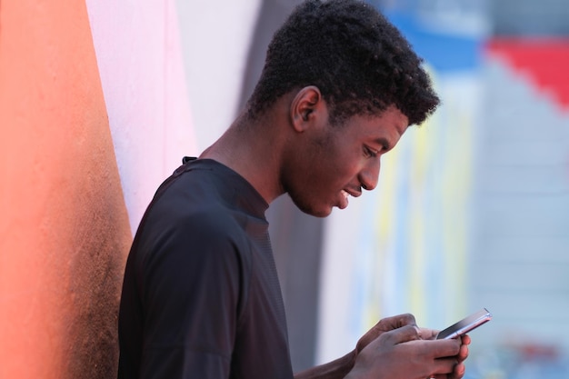 Ritratto di giovane con i capelli ricci che guarda lo smartphone sorridente