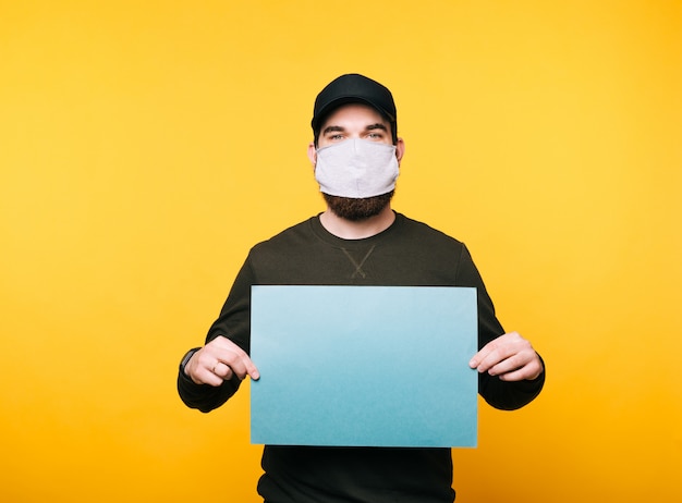 Portrait of young man with facial mask holding blank paper