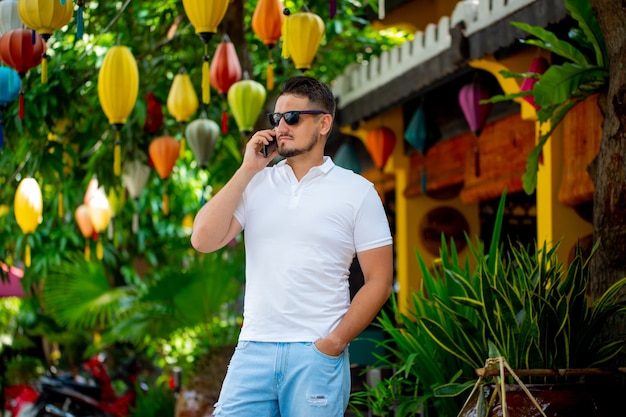 Foto ritratto di un giovane uomo con gli occhiali che cammina all'aperto con un telefono cellulare. un uomo con un telefono. una persona felice sta parlando al telefono.