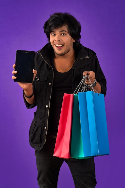 Portrait of a young man with a mobile phone or tablet smartphone and shopping bags in his hands