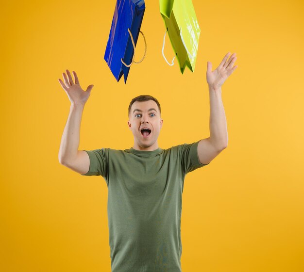 Portrait of young man with paper bags on yellow background. Space for text