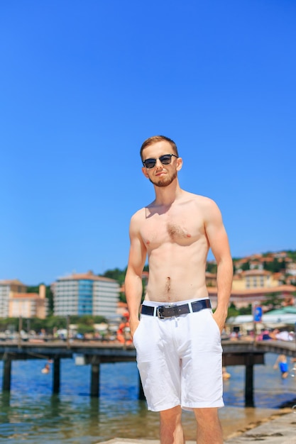 Portrait of young man with sexy body in shorts and sunglasses p