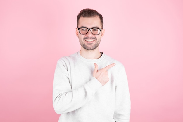 Portrait of a young man with a smile points his index finger towards copyspace