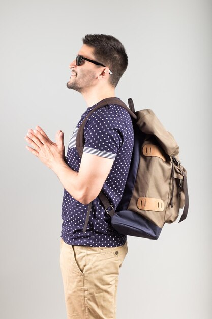 Portrait of a young man with sunglasses and backpack isolated on gray background