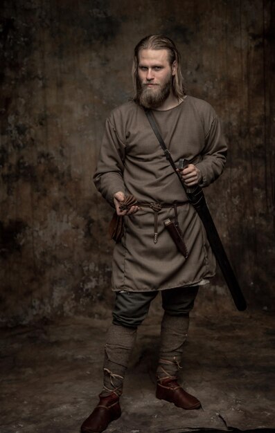 Photo portrait of young man with sword standing against wall