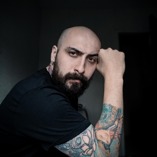 Portrait of young man with tattoo sitting against wall