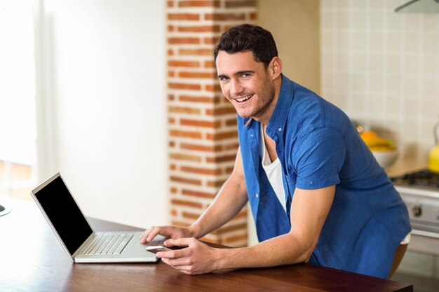 Ritratto del giovane che lavora al computer portatile in cucina