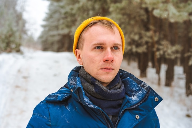 Portrait of a young man in a yellow hat in a snowy winter forest, Christmas holidays