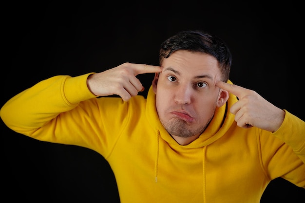 Portrait of young man in yellow hoodie with grimacing face Close up of funny guy monkeying on black background