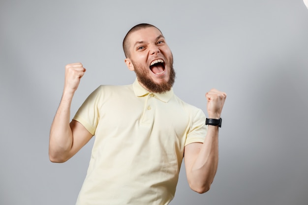 Portrait of a young man in a yellow T-shirt rejoices in victory on gray.