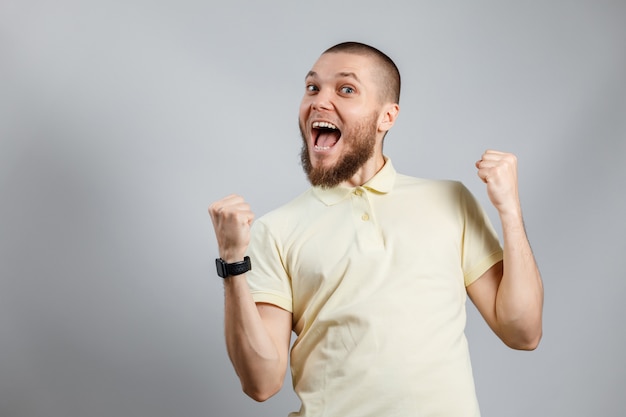 Portrait of a young man in a yellow T-shirt rejoices in victory on gray.