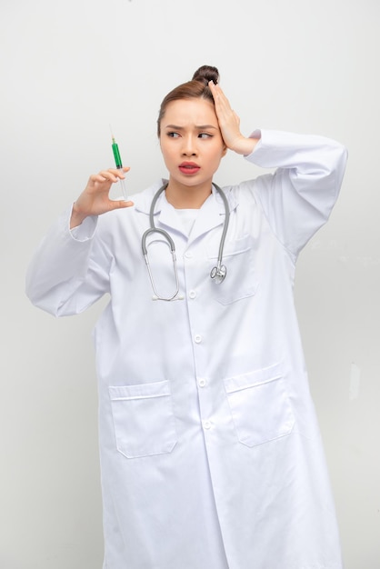 Portrait of young medical nurse looking suspiciously at syringe isolated on white background with copyspace advertising area