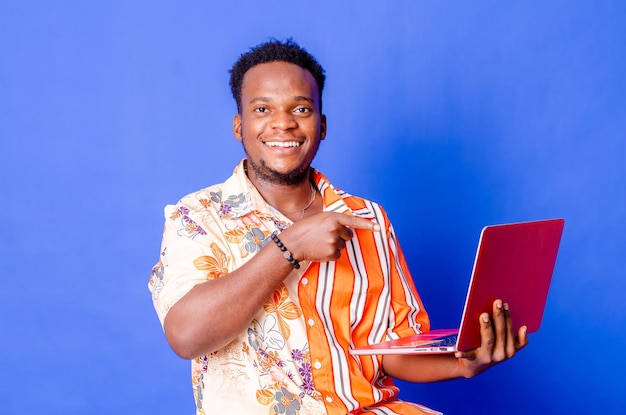 Portrait of young modern businessman standing holding laptop and looking at camera with happy smile