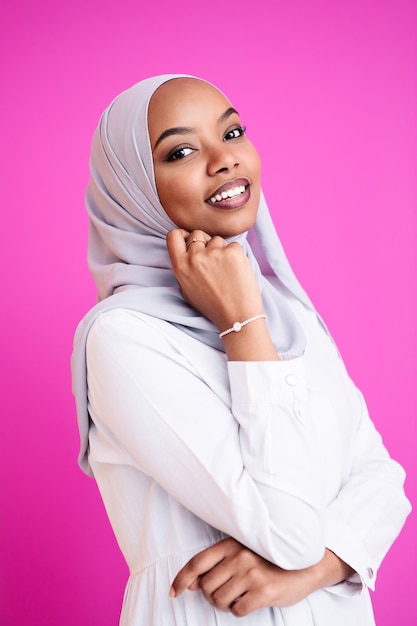 портрет молодой современной мусульманской афро красавицы в традиционной исламской одежде на пластиковом розовом фоне