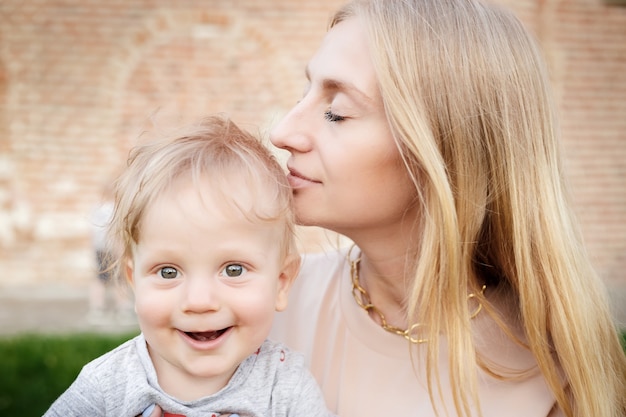 Photo portrait of young mom with blond baby outdoors. happy family. mum with baby.