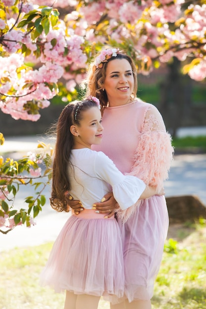 Portrait of a young mom with her daughter standing under a sakura Beautiful mom and daughter wearing same clothes