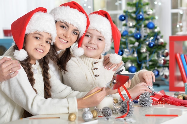 Portrait of young mother and her children making Christmas decorations sitting at the table