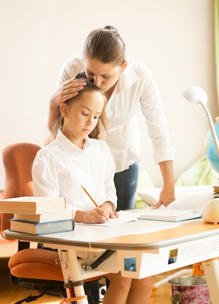 Portrait of young mother hugging and praising daughter while doing homework