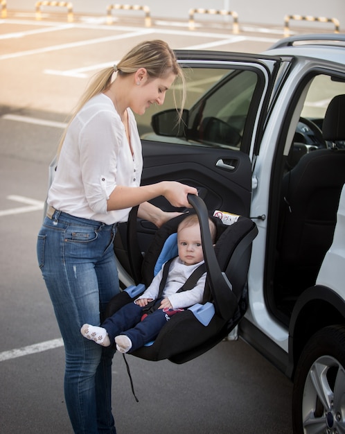 Photo portrait of young mother installing car child seat with baby