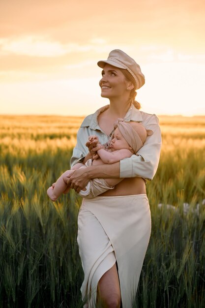 A portrait of young mother with a baby in her arms at sunset in the field happy family concept