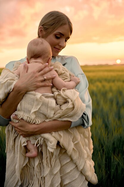 A portrait of young mother with a baby in her arms at sunset in the field happy family concept