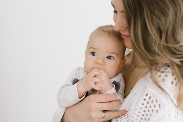 Portrait of a young mother and a young son. a mother holds her\
baby in her arms. the baby keeps his hands in his mouth. happy\
motherhood and childhood