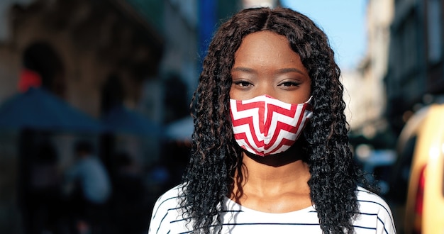 Photo portrait of young multiracial woman wearing protective medical mask on her face looking at camera ag...