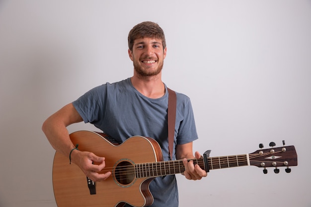 Portrait of a young musician who plays the guitar and smiles.  Artist isolated on white wall. Young smiling man.