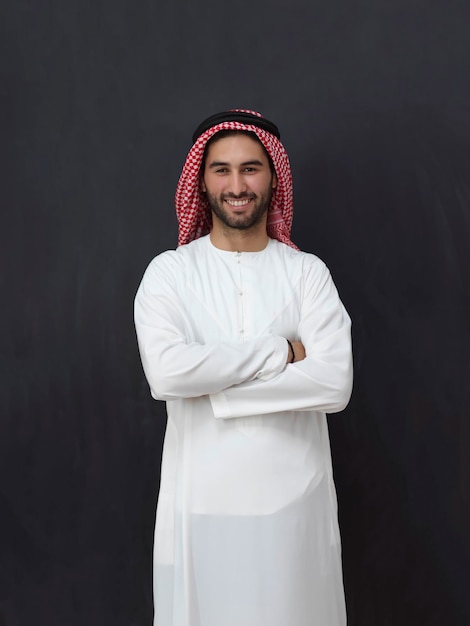 Portrait of young muslim man wearing traditional clothes. Happy Arab standing in front of black chalkboard representing Ramadan Kareem concept