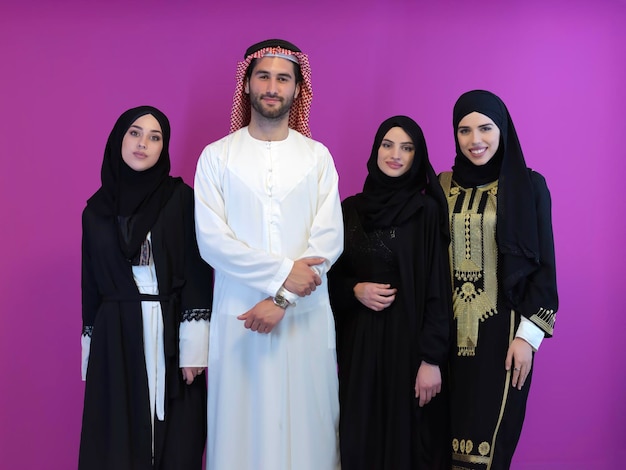 Portrait of young muslim people in traditional clothes. Happy arabic family together, man and three women isolated on pink background