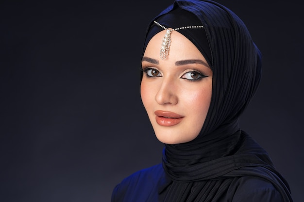 Portrait of a young muslim woman in hijab on black surface