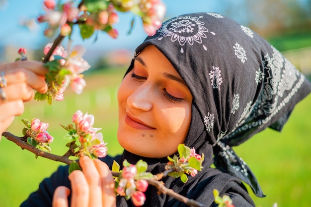 Foto ritratto di una giovane donna musulmana in piedi sull'erba tra ciliegie selvatiche in fiore