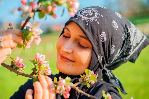 Portrait of a young Muslim woman standing on the grass among blossoming wild cherries