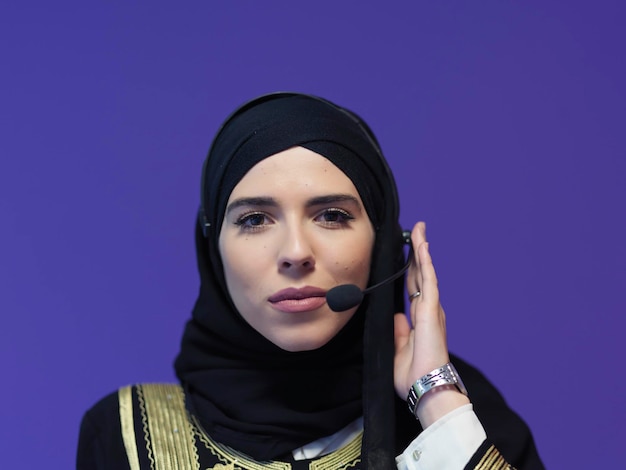 Portrait of young muslim woman with headphones working as call center operator isolated on purple background