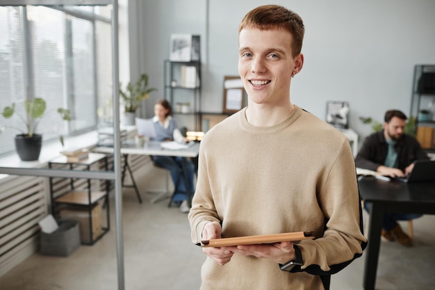 Portrait of young office worker holding digital tablet smiling at camera while working at office