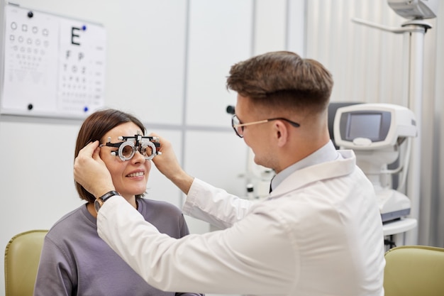 Photo portrait of young ophthalmologist putting trial frame on smiling female patient