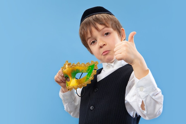 Portrait of a young orthodox jewish boy with carnival mask isolated on blue studio