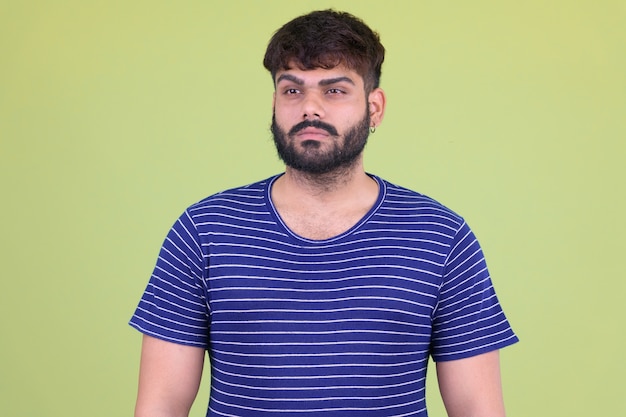 Portrait of young overweight bearded Indian man against colored wall