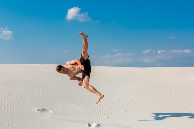 Ritratto di giovane uomo di parkour che fa capovolgimento o capriola sulla sabbia.