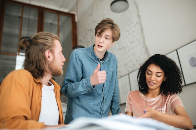 Portrait of young people discussing something in office. Two boys with blond hair and girl with dark curly studying together in classroom