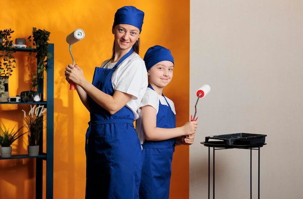 Portrait of young people painting orange walls with paintbrush\
roller and color, using diy renovating tools to redecorate\
apartment room. woman with small kid doing paint job improvement at\
home.