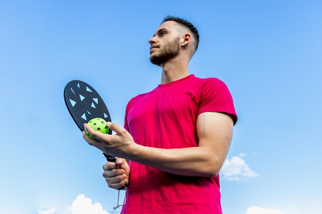 Photo portrait of a young pickleball player holding the paddle and ball against the backdrop of a blue sky