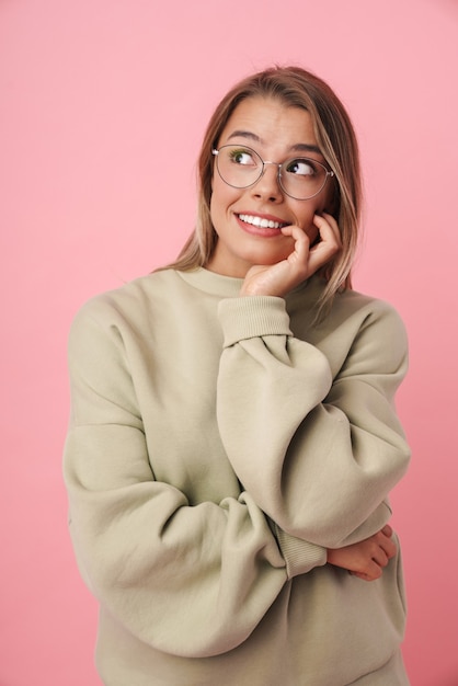 Portrait of young pleased woman in eyeglasses looking aside and smiling isolated on pink
