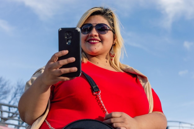 Photo portrait young plus size caucasian latin woman smiling checking phone outdoors