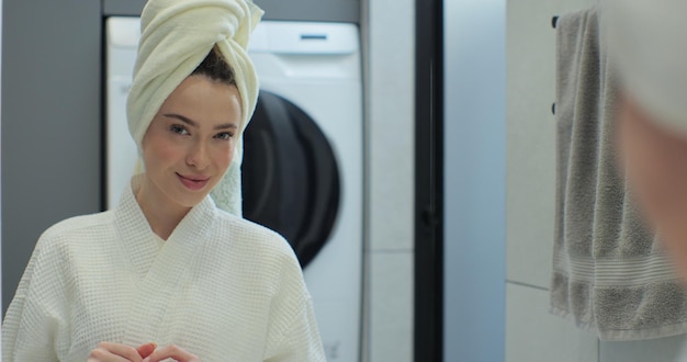 Foto ritratto di una giovane donna positiva che indossa un accappatoio e un asciugamano sulla testa dopo la doccia sorridendo