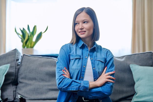 Portrait of young positive woman with arms crossed in living room